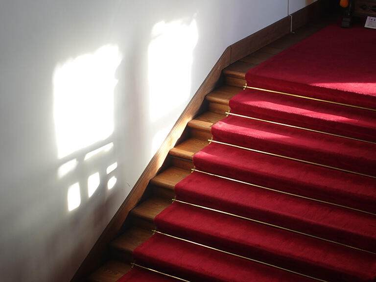 赤絨毯が敷かれた階段に差し込む日の光が美しい